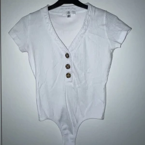 Vit body - Vit t-shirt body från Missguided. Bra skick, använd kanske 5 ggr. Fin lagom urringning. När man har den på sig ser det ut som en skin-tight instoppad tröja.