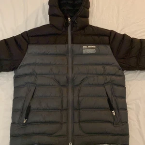 Axel Arigato  - Hyde Bi-Color Hooded Puffer Jacket från Axel Arigato. En grå svart jacka som är använd under en vår. Den är slutsåld och var nypris 3500