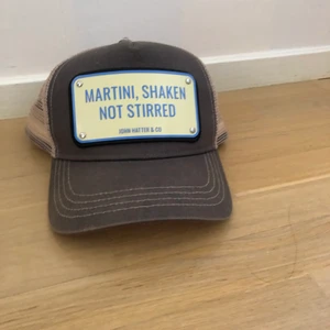 John hater keps - John hater keps motiv martini,shaken not stirred. Nyskick den är i princip oanvänd. Boxen följer med nypris 990 kr