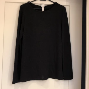 Tröja med omlottrygg - En stickad tröja i mjuk kvalitet med omlottlagt bakstycke i svart färg, storlek M.  Fraktkostnaden är inkluderat i priset. 