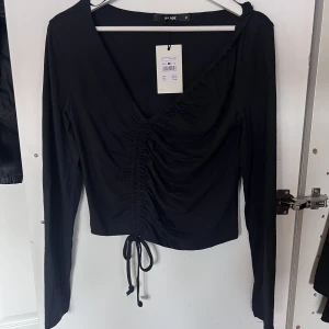 Svart topp - En svart topp med rysh fram från BikBok. Storlek M, aldrig använd, endast provad. Alla lappar sitter kvar