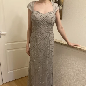 Grå långklänning med detaljer  - Elegant märkeslångklänning. Vackra pärldetaljer längs hela. Skickar fler bilder vid intresse. Orginalpriset är 2400 kr.
