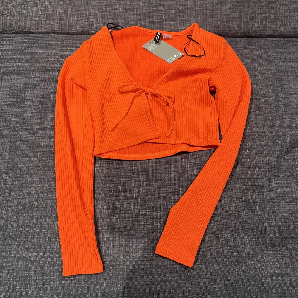Orange topp med knytning fram från H&M. Aldrig använd prislappen kvar, storlek XS.. Tröjor & Koftor.