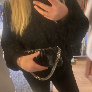Svart väska med kedja - En svart väska med ormsskin och lack imitation med en tjock kedja som väskbannd. Från asos och sparsamt använd med ett fint skick💕hör av er för frågor eller fler bilder!
