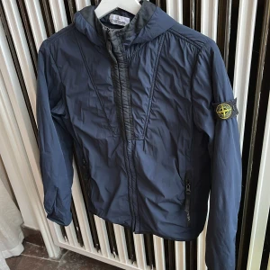 Stone island jacka, Blå - Denna jacka är i en fin unik blå färg. Jackan är i storlek 142 cm men funkar även för 150. Denna jacka änvände jag knappt under den tiden jag kunde ha den, därav är skicket 9/10 utan skador eller märken.