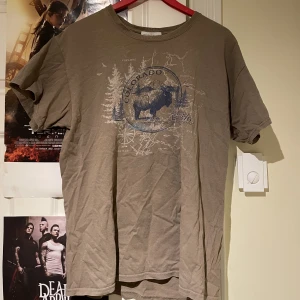 T-shirt - En brun/biege t-shirt med ett tryck på framsidan. Trycket föreställer en oxe och skog.