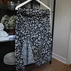 Blommig kjol i svart med slits  - En såå vacker kjol i svart med vita blommor. Slits med dragsko som kan justeras. I sidan finns en dragkedja. Andra bilden visar modellen men den som säljs i denna annons är svart!  Storlek M men passar mer en S.  Frakt ingår i priset!!🚚📦