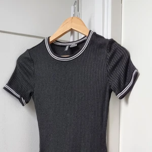 Divided svart ribbad klänning 34 - Klänningen är en tajt fit för en rolig natt ute, men också till kafé dejtar. Ribbad och stretchig med vida detaljer runt kragen och armar. 