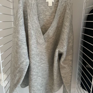 Stickad tröja - Grå stickad tröja som passar perfekt nu till vintern. Den har en V ringad krage som gör så att man kan ha den hängandes ner över axeln, eller som en urringning. 