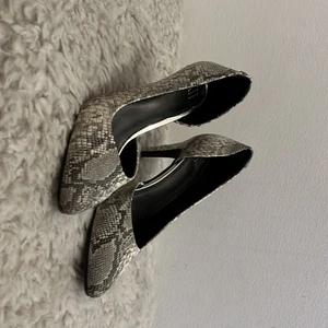 Ormskinnsmönstrade klackskor - Vit/grå klackskor med spetsig tå, ormskinnsmönster. Ca 7 cm klack.  