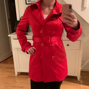 Trenchcoat från Orsay stl 38 - En av mina favoritjackor 😍 Röd trenchcoat i diskret skimrande material; 55% bomull/ 41% / 4% elastan. Lite häftigt foder samt innerficka. Dubbelknäppt med detaljer bak och axlar. Skärp i midjan. Fint begagnat skick ❤️ Storlek 38, lite mindre i modellen som passar mig rätt bra som står mellan 36-38 i jackor (byst ca 90 cm). 