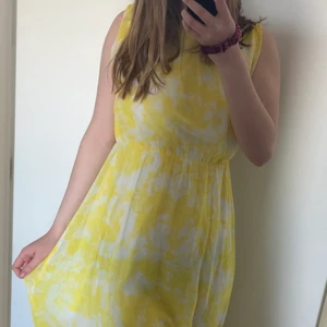 Gul långklänning med slits  - Gul och vit långklänning med två slits. Tyget är tunt, jätteskönt på sommaren! Undertyget gör att den inte är genomskinlig. Öppen i ryggen.