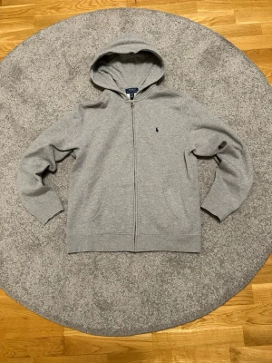 Grå zip hoodie Polo Ralph Lauren - Klassisk grå hoodie med dragkedja från Polo Ralph Lauren. Väldigt fint skick i storlek XL kids passar som saml. Hör av dig vid frågor
