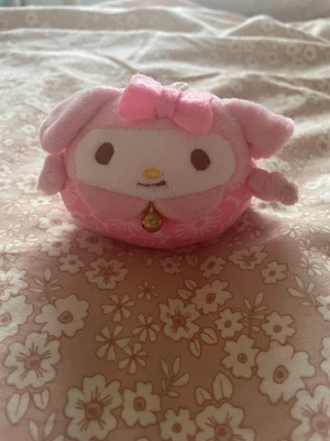 My Melody mjukisdjur nyckelring - Söt My Melody mjukisdjur i rosa plysch med vita blommor, rund form och små öron. Har en rosa rosett på huvudet och en liten bjällra under hakan. Perfekt som dekoration eller nyckelring.