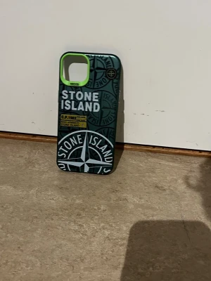 Grönt Stone Island mobilskal - Snyggt mobilskal i mörkgrönt med Stone Island-logga och kompassmönster. Skalet har en cool limegrön kant runt kamerahålet och detaljer i vitt och gult. Tillverkat i tåligt plastmaterial och passar perfekt för dig som vill ha en unik look på mobilen.