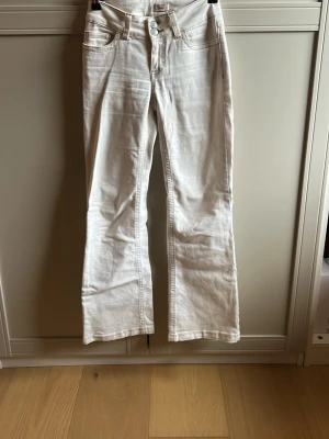 Vita bootcut jeans med brodyr - Säljer ett par vita bootcut jeans med snygg brodyr på bakfickorna och dubbla knappar i midjan. Jeansen har klassisk femficksdesign och är tillverkade i ett stretchigt denimtyg som sitter bekvämt. Perfekta för dig som vill ha en fräsch och trendig look. Jeansen är uppsydda men passar någon som är 166cm.❤️❤️