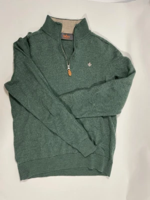 Grön halvzip tröja med brodyr - Grön tröja med halv dragkedja och liten broderad detalj på bröstet. Tröjan har ribbade muddar vid ärmslut och nederkant samt hög krage. Perfekt för lager på lager och chill stil.
