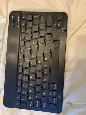 Svart trådlöst tangentbord - Säljer ett kompakt svart trådlöst tangentbord med QWERTY-layout. Tangentbordet har låg profil och smidiga knappar, perfekt för att koppla till surfplatta eller dator via Bluetooth. Tillverkat i plast och har strömbrytare samt laddningsindikator.