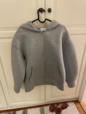 Grå zip hoodie från Kappahl (Teddy Jacka) - En stilren grå hoodie med dragkedja från Kappahl. Hoodien har en klassisk huva, två fickor framtill och ribbade muddar vid ärmslut och nederkant. Perfekt för en avslappnad och enkel look. Materialet känns mjukt och bekvämt. Nästan helt ny. Använt den en gång
