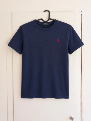 Polo Ralph Lauren T-shirt navy – M (10–12 år) 🐎 - Klassisk mörkblå T-shirt från Polo Ralph Lauren med röd broderad logga på bröstet. Enkel och tidlös modell som passar till det mesta. 🔹 Storlek: M (10–12 år) 🔹 Färg: Mörkblå / navy 🔹 Broderad röd Ralph Lauren-logga 🔹 Fint begagnat skick utan defekter! Säljes då den inte längre kommer till användning. Hör gärna av dig vid frågor eller om du vill ha mått! 💌