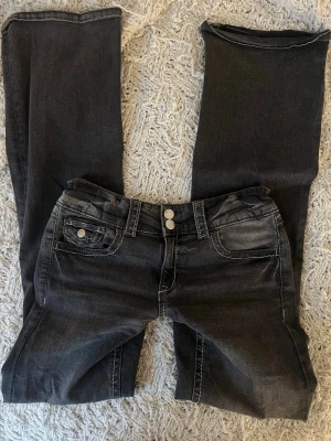 Svarta bootcut jeans från Gina Tricot - Snygga svarta bootcut jeans från Gina Tricot med dubbla silverknappar och klassiska fem fickor. Jeansen har en tvättad look med ljusa partier och kontrastsömmar. Perfekta för dig som gillar en avslappnad men trendig stil.