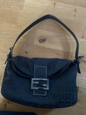 Fendi Zucca Väska  - Fendiväska köpt på a retro tale! Väskan har ett stort metallspänne framtill och lockstängning. Materialet ser ut att vara tyg med detaljer i läder. Perfekt för dig som gillar klassisk men trendig stil.