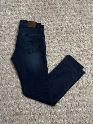 Mörkblå sand jeans - Snygga mörkblå jeans med klassisk femficksdesign och raka ben. Jeansen har en läderpatch bak i midjan och är tillverkade i ett slitstarkt denimtyg. Perfekta för en avslappnad och trendig look.