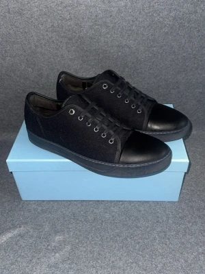 Svarta låga sneakers från Lanvin - Stilrena svarta sneakers med lågt skaft i mocka från lanvin. Skorna har svarta snören och metallfärgade öljetter. Perfekta för en clean och enkel look.