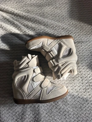 Beiga höga sneakers med kilklack - Unika sneakers i beige mocka och textil med högt skaft och kilklack. Skorna har flera kardborreband och detaljerade paneler, samt en brun gummisula. Perfekta för dig som vill sticka ut med en cool och trendig look. Köparbevis finns!!!!