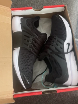 Nike svarta mesh sneakers prestos - Säljer ett par svarta Nike sneakers med mesh-överdel och vita sulor. Skorna har en sportig look med plastdetaljer på sidorna och klassisk Nike-logga. Perfekta för dig som gillar stilrena och bekväma sneakers.