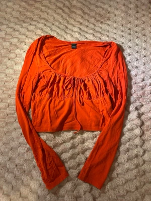 Röd croppad topp från SHEIN - Trendig röd långärmad topp från SHEIN med croppad passform och snygg snörning framtill. Tillverkad i mjukt material som känns skönt mot huden. Perfekt för dig som vill ha en färgstark och modern look.