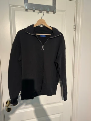 Svart half-zip hoodie Jack & Jones - Svart hoodie från Jack & Jones med halv dragkedja och hög krage. Klassisk och enkel design utan tryck, tillverkad i mjukt material. Perfekt för chill dagar eller när du vill ha en clean look. Ribbade muddar vid ärmslut och nederkant.