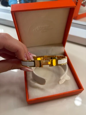 Vitt och guldigt armband  - Snyggt armband  i vitt och guldigt metall. Armbandet har den ikoniska detaljen framtill och kommer i ask. Perfekt accessoar för att lyfta din outfit med en lyxig touch. Armbandet är helt nytt och aldrig använt.