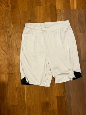 Vita sportiga Puma shorts med svarta detaljer - Snygga vita shorts med svarta detaljer vid bensluten. De har elastisk midja och är tillverkade i ett lätt och svalt material som passar perfekt för träning eller sport. Klassisk och enkel design som funkar till det mesta.