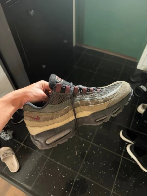 Nike Air Max 95 olivgrön/brun - Säljer ett par Nike Air Max 95 sneakers i olivgrönt och brunt med svarta och vinröda detaljer. Skorna har en chunky sula med synliga Air-enheter och mesh- samt mockapaneler för en sportig look. Klassisk Nike Swoosh på sidan och snörning med vinröda öglor.