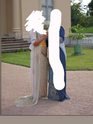 Kurdisk klänning - Säljer en elegant långklänning i guld med glittriga paljettdetaljer och transparent tyg. Klänningen har en omlottkänsla, markerad midja och halvtransparenta ärmar. Perfekt för dig som vill sticka ut med en lyxig look.