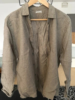 Beige linneskjorta från Intimissimi - Säljer en beige långärmad skjorta från Intimissimi Uomo i svalt och luftigt linne. Skjortan har klassisk krage, knappar framtill och en avslappnad passform. Perfekt för dig som gillar stilrena och enkla plagg.