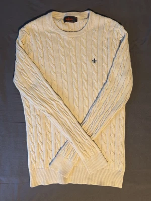 Beige kabelstickad tröja Morris - Kabelstickad tröja i beige från Morris med rund halsringning och ribbade muddar. Tröjan har ett diskret Morris-emblem broderat på bröstet och är tillverkad i ett mjukt material som passar perfekt för kyligare dagar. Säljer då den är lite för stor för mig