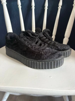 Svarta sneakers med platåsula - Säljer ett par svarta sneakers med bred platåsula och snörning. Ovandelen är i sammetsliknande material som ger en cool och unik look. Perfekta för dig som vill sticka ut och få lite extra höjd. Passar till många olika stilar.