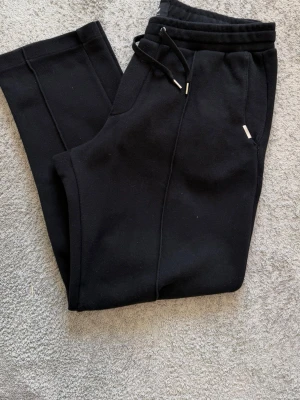 Svarta mjukisbyxor från H&M - Svarta mjukisbyxor från H&M med regular fit. Byxorna har dragsko i midjan, sidofickor och raka ben. Tillverkade i mjukt bomullsmaterial som är skönt mot huden. Perfekta för chill dagar eller när du vill ha det bekvämt.
