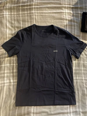 Mörkblå BOSS t-shirt i bomull - Snygg mörkblå t-shirt från BOSS i mjuk bomull. Klassisk passform med rund halsringning och diskret BOSS-logga på bröstet. Perfekt till jeans eller shorts för en clean och stilren look.