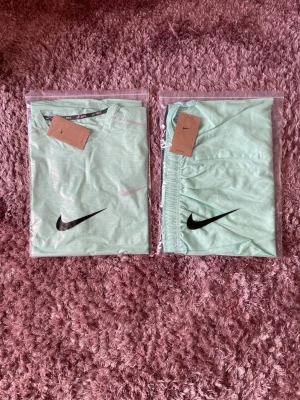 Mintgrönt Nike träningsset - Stolen XL men passar också L.                                        Säljer ett fräscht mintgrönt träningsset från Nike med t-shirt och shorts. Båda plaggen har tydliga svarta Nike-loggor och är tillverkade i ett lätt och svalt material som passar perfekt för träning eller sportaktiviteter.