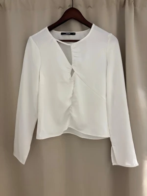 Vit långärmad blus från BikBok - Stilren vit blus från BikBok i storlek XS. Blusen har lång ärm, rund halsringning och en unik omlott-design framtill med lätt rynkning. Tillverkad i ett mjukt, tunt tyg som ger en elegant look. Perfekt att matcha med jeans eller kjol. Använd 1 gång. Köparen står för frakten💕