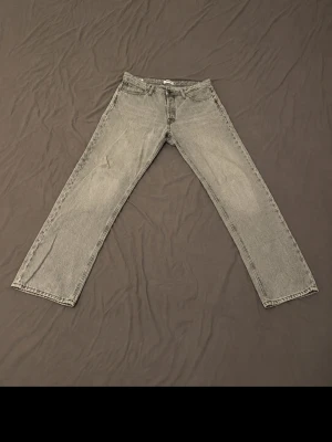 Grå raka jeans med vintagekänsla - Säljer ett par grå jeans med rak passform och klassisk femficksdesign. Jeansen har en snygg vintagekänsla och subtila slitningar. Materialet är kraftig denim i bomull och bakfickan har en diskret dekorsöm. Perfekta för en avslappnad och trendig look.