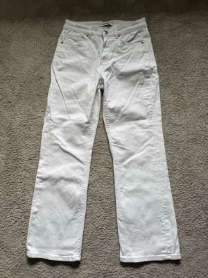 Vita raka jeans - Säljer ett par vita jeans med rak passform. Jeansen har hällor för skärp och stängs med knapp och dragkedja. Perfekta för en clean och fräsch look. Materialet är denim.