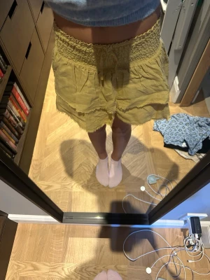 Gula volangshorts med smock - Ljusgula shorts med bred smock i midjan och dubbla volanglager. Shortsen har råa kanter och en lös, flowy passform som ger en chill vibe. Tillverkade i ett tunt, luftigt material som passar perfekt till sommaren.