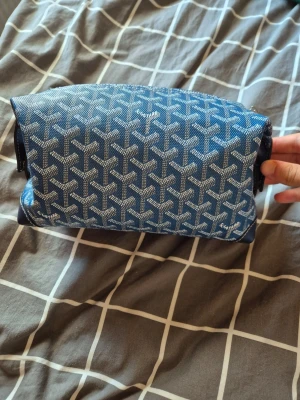 Blå necessär med mönster - Snygg blå necessär med vitt grafiskt mönster och dragkedja upptill. Väskan har en rektangulär form och är perfekt för att förvara smink, hygienartiklar eller småprylar. Tillverkad i ett tåligt material med stilren design.