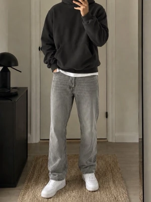 Mörkgrå hoodie med huva - Säljer en mörkgrå hoodie med klassisk huva och stor magficka framtill. Hoodien har en avslappnad passform och är tillverkad i mjukt material som känns skönt mot huden. Perfekt för en chill och enkel stil.