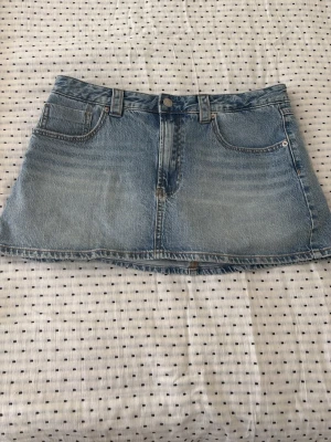 Blå jeanskjol från Stradivarius - Säljer en klassisk blå jeanskjol från Stradivarius i modell kortkjol. Kjolen har fem fickor, bälteshällor och stängs med knapp och dragkedja framtill. Perfekt till sommaren och enkel att matcha med olika toppar.