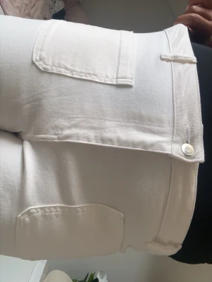 Vita raka jeans med stora fickor - Snygga vita jeans med raka ben och stora, markerade fickor både fram och bak. Jeansen har hög midja och stängs med knapp och dragkedja. Perfekta för en clean och fräsch look. Materialet är klassisk denim i bomull.
